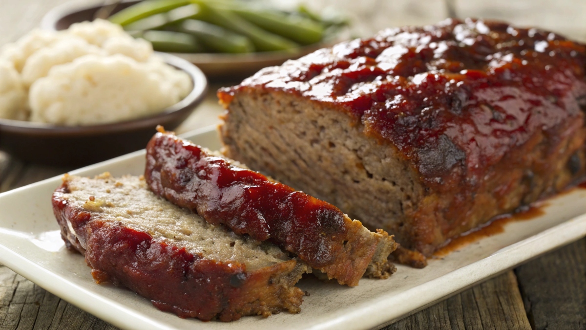 A perfectly glazed meatloaf with a rich, homemade meatloaf sauce, served with mashed potatoes and green beans.